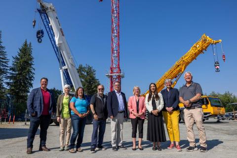 Nine people standing in front of three tall tower cranes